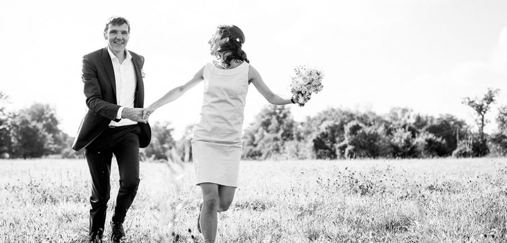 Brautpaar läuft glücklich über eine Wiese.